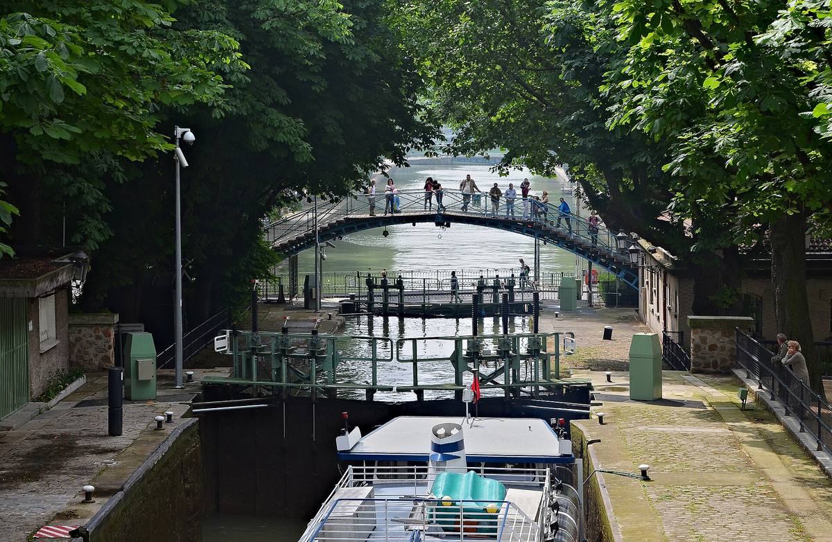 Une écluse du canal Saint-Martin à Paris, surmontée d'une passerelle en fer et bordée d'arbres