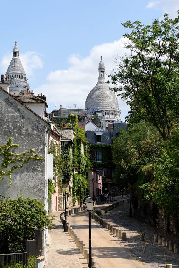 La rue de l'Abreuvoir à Montmartre, pavée et bordée de maisons, avec les dômes du Sacré-Cœur au fond